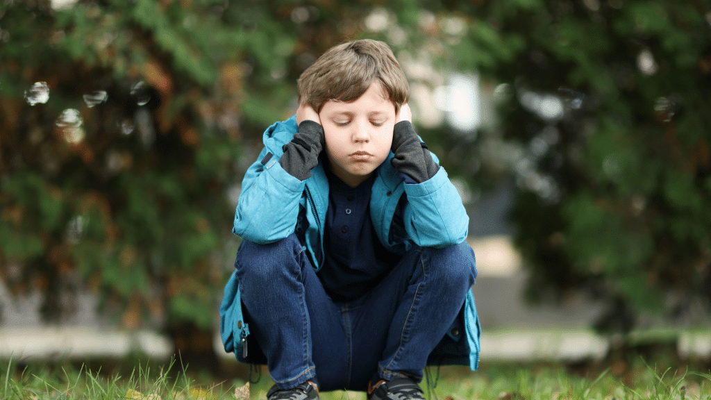Child outside holding hands over ears