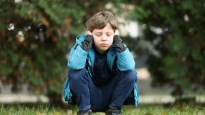 Child outside holding hands over ears
