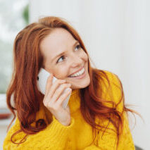 Portrait of smiling red-haired woman wearing yellow sweater talking on phone