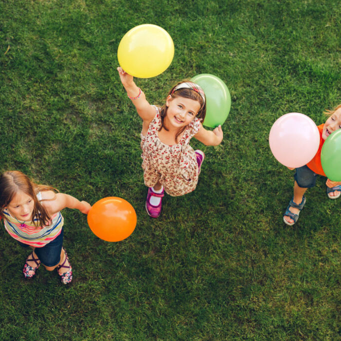 Three happy little kids playing with colorful balloons outdoors, top view