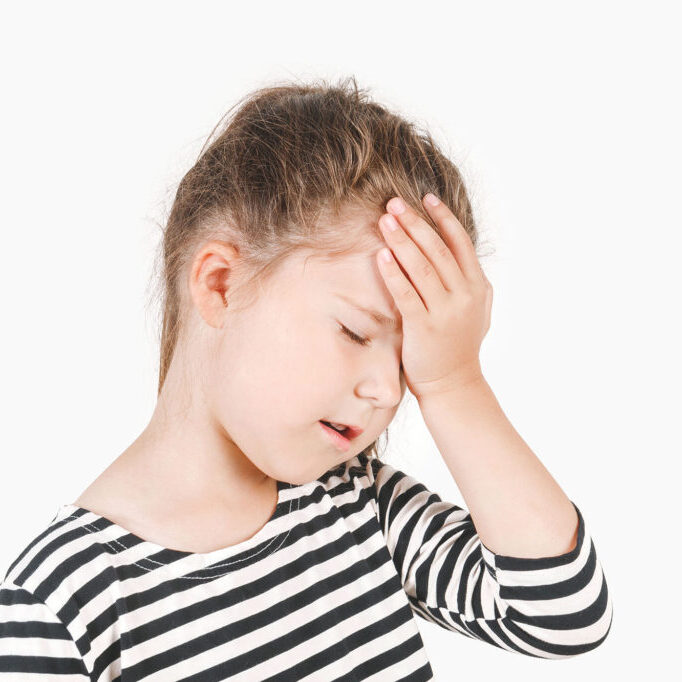 Facepalm. Upset girl with closed eyes and hand holding on her forehead. Frustrated forgetful girl with head tilted forward down. Posing a little girl wearing a striped shirt. Isolated background.