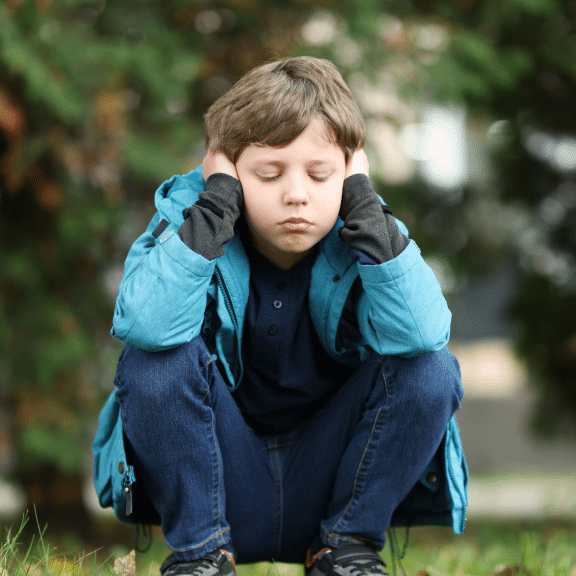 Child outside holding hands over ears