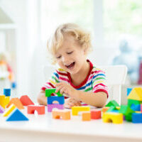 Kid playing with colorful toy blocks. Little boy building tower of block toys. Educational and creative toys and games for young children. Baby in white bedroom with rainbow bricks. Child at home.